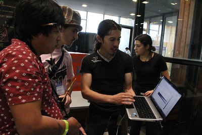 Photo of attendees gathering around a another attendee who is holding a laptop and presenting to the group.